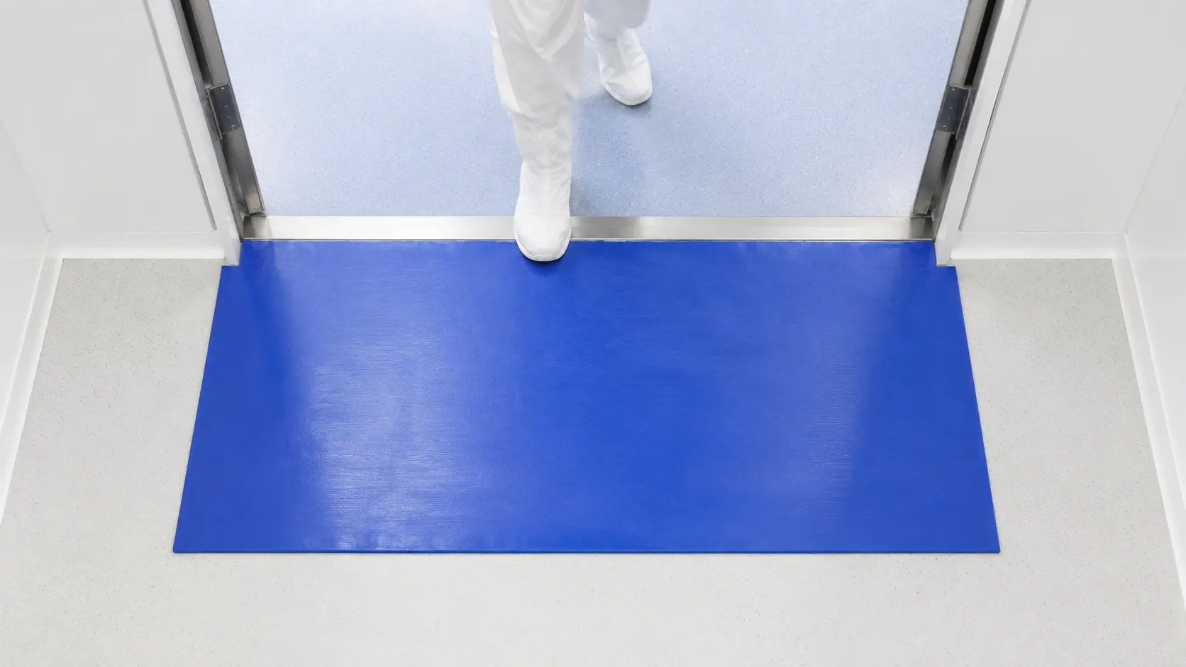 Overhead view of a cleanroom entrance showing the correct placement of a large blue sticky mat covering the full doorway width.